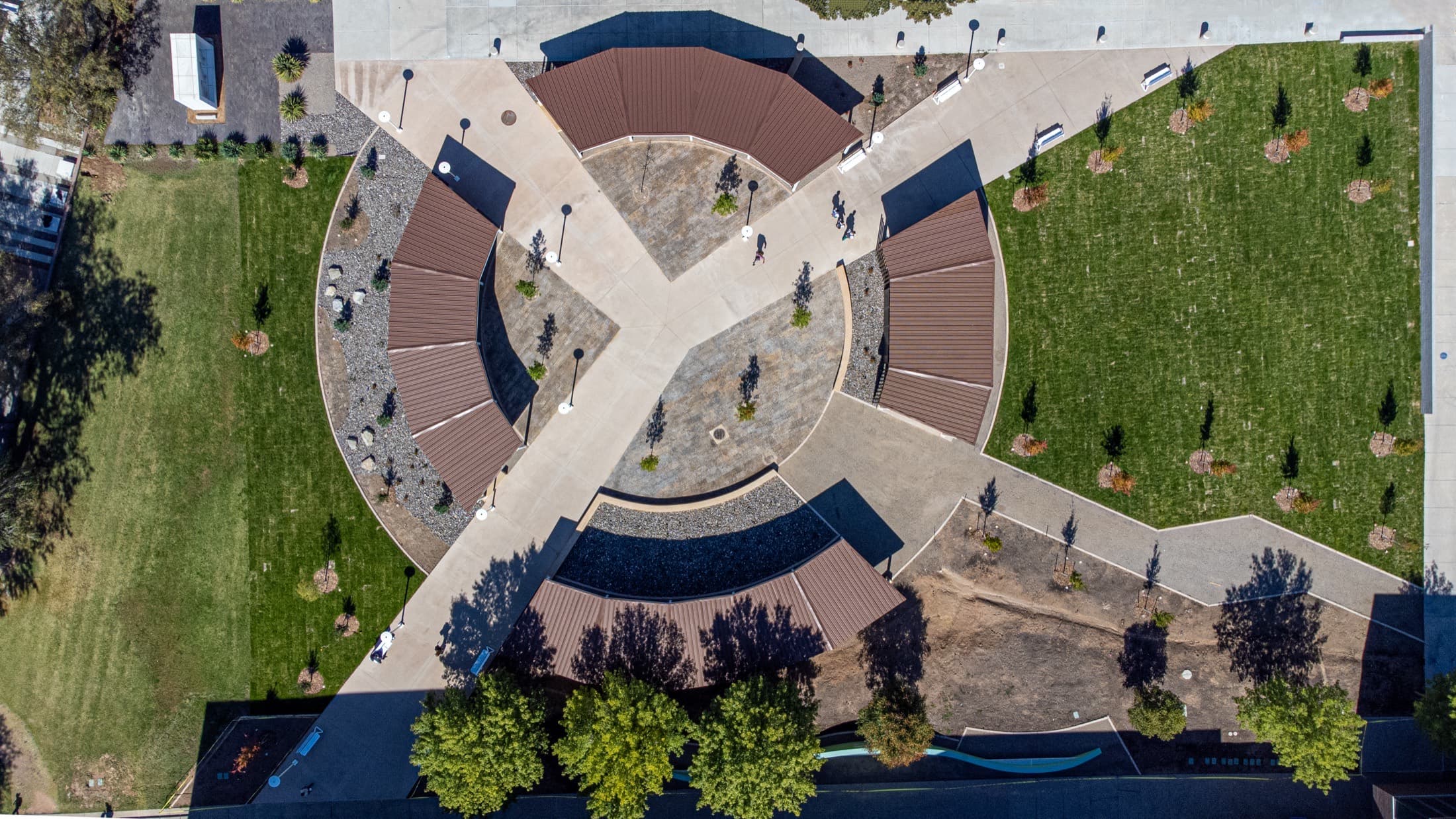Straight-down aerial of a round campus courtyard, crossing paths and curved shade canopies