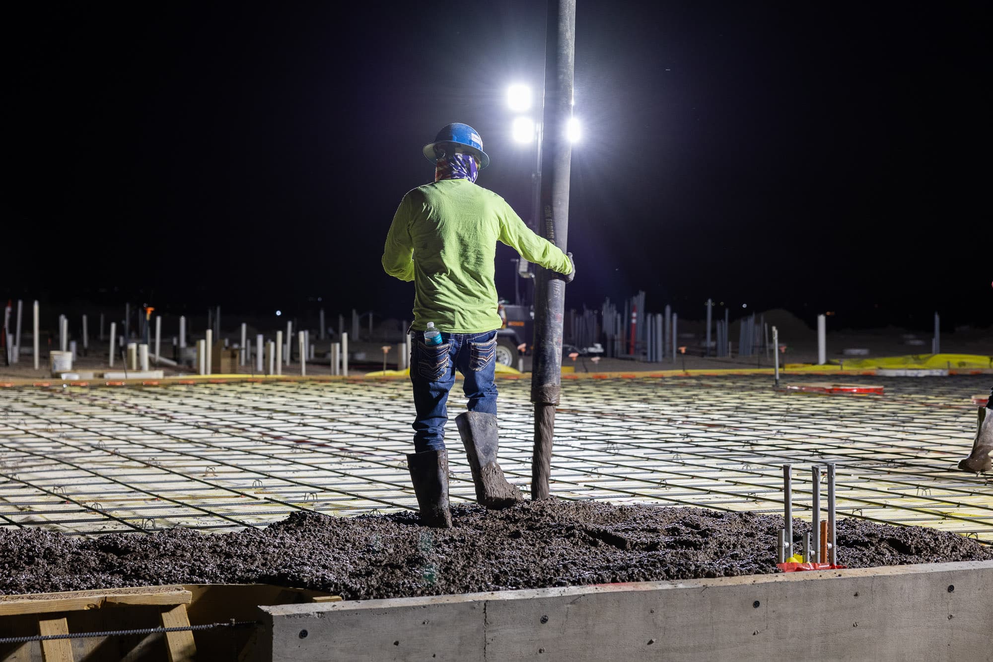Worker guiding a concrete pour under light towers at night